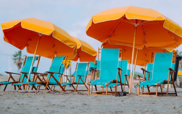 a group of empty teal beach chairs under orange umbrellas on a sunny day