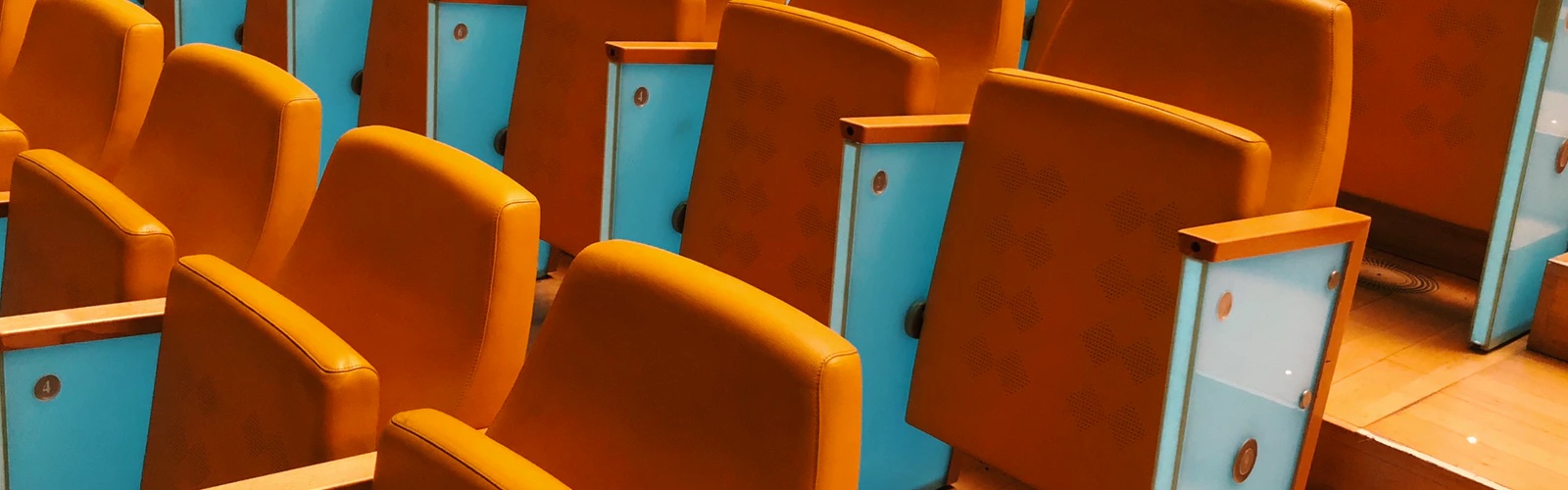 rows of empty, orange padded auditorium seats with teal accent panels on the arm rests