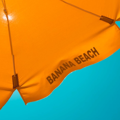 section of an orange beach umbrella with the words'Banna Beach' on the edge, against a bright blue sky